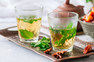 Traditional moroccan mint tea with dates on a vintage tray. White stone background.
