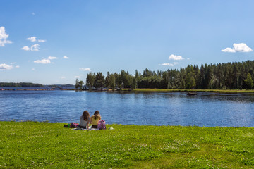 Obraz na płótnie Canvas Two girl are resting on lake shore, sunny day