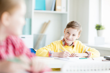 Smiling secondary schoolboy looking at his classmate at lesson during group discussion