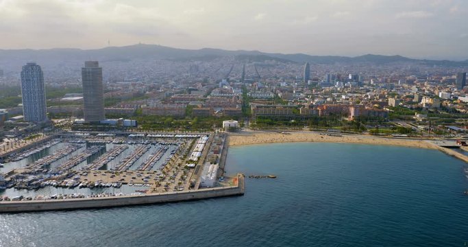 Flying along Barcelona shore with city skyline, Spain. Aerial view with afternoon light