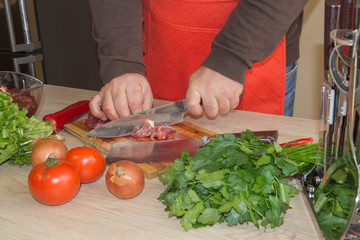 a man in a kitchen apron, meat on a board and a wooden table