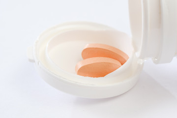 Heap of tablets medicine lying beside of plastic bottle. Pills and bottles are white. Isolated on white