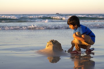 Child playing with sand at beach. Kid building sand castle with sea waves around and background. Shot in evening golden hour © Anjuman