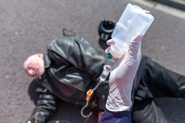 German ambulance service person holds an infusion near an injured biker