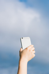 A female holding mobile phone against blue sky background.