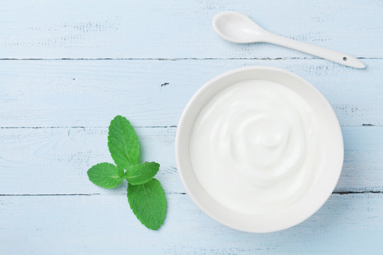 Greek yogurt in bowl decorated mint leaf on blue rustic table top view.