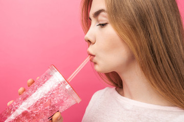 Portrait of beautiful young woman drinking fizzy drink from a bottle with a straw and looking at...
