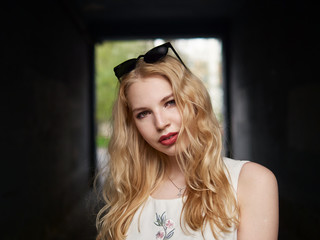 Close up of blonde student girl with trendy sunglasses posing in arc, enjoying warm sun light, recreation and relaxation on spring holiday