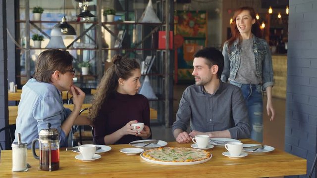Pretty young girl is meeting her friends in pizza house doing high five and talking to mates drinking tea. Friendship, modern lifestyle and eating out concept.