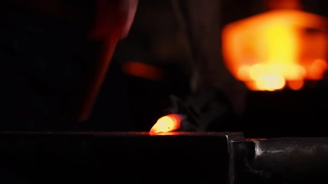 Get out of the furnace hot metal to make a sword war. Master of ancient art creates metal products. In slow motion blacksmiths hammer on red metal flying sparks.