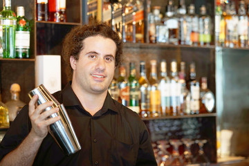 Professional bartender man holding in hands a shaker with a fresh delicious cocktail. Bartender shaking a cocktail shaker as she stands behind the bar mixing a drink for a client. Toning