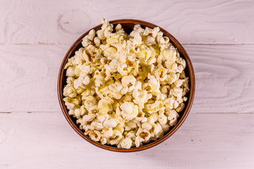 Ceramic bowl with popcorn on wooden table. Top view
