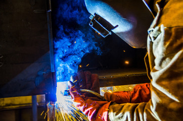 The worker in overalls and a protective mask welds metal with a welding machine. Profession welder....