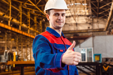 A man is showing his thumb up. An employee in overalls and a white helmet of an industrial plant shows a class. Gestures.