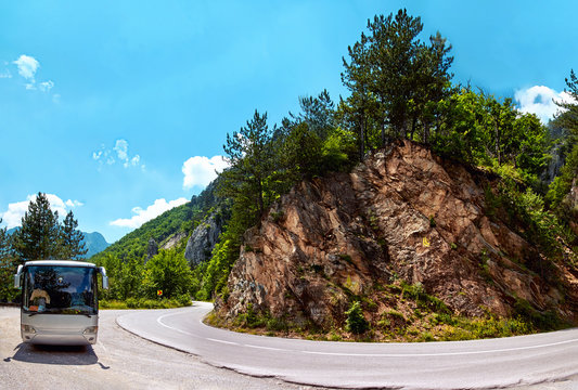 Tourist excursion bus on the dangerous serpentine mountain road stopped at on the sanitary stop. Montenegro. Wide-angle view of a winding road in the mountains