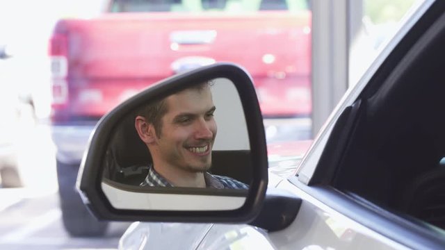 Shot of a handsome male driver smiling joyfully sitting in a car, close up of a side mirror of an automobile. Driving new car. Happy male customer in a new auto. Rental service concept.