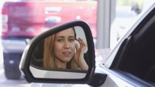 Close up shot of a side mirror of a car, gorgeous young woman smiling joyfully sitting in her new automobile. Transportation vehicles. Safe driving. Automotive business concept.