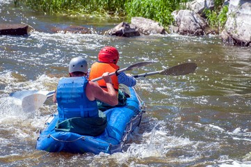 Rafting, kayaking. Two sportsmen in sports equipment are sailing on a rubber inflatable boat in a boiling water stream. Teamwork. Water splashes close-up. Extreme sport.