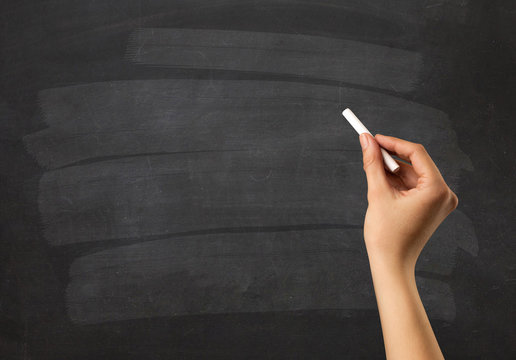 Female hand holding white chalk in front of a blank blackboard