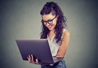 Cheerful young woman holding and using laptop