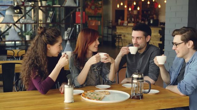 Friends are celebrating reunion in cafe over drinks and pizza, clanging cups, drinking and sharing news. Friendship, modern lifestyle, communication and celebration concept.