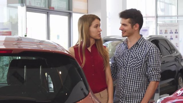 Attractive woman and her handsome boyfriend choosing a new automobile at the dealership salon. Cheerful couple shopping for a new auto. Travelling, relationships, investment concept.