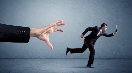 Young miniature businessman running from a big hand with blue background