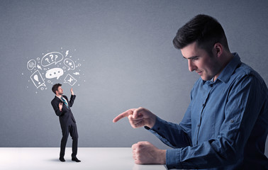 Young professional businessman being angry with an other miniature businessman who has drawn speech and thought bubbles above his head