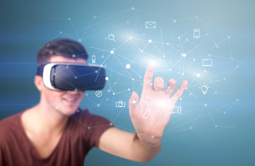 Young impressed man wearing virtual reality goggles with mixed media icons around his finger