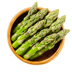 Fresh green asparagus tips in wooden bowl. Sparrow grass shoots. Cultivated Asparagus officinalis. Vegetable with thick stems and closed buds. Isolated macro food photo close up from above over white.