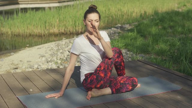 Attractive brunette doing yoga twist in morning sunlight near grass