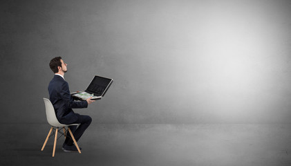 Businessman staying in an empty grey dark room with stuffs on his lap
