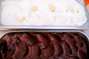 The combination of black chocolate and white chocolate creamy ice cream packed in steel service containers on the table. Industrial preparation of creamy ice cream. Pastry shop.