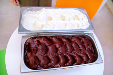 The combination of black chocolate and white chocolate creamy ice cream packed in steel service containers on the table. Industrial preparation of creamy ice cream. Pastry shop.