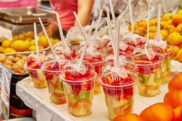 Fototapeta na wymiar Sliced mandarin, strawberry, kiwi and melon in a glass at a street food market