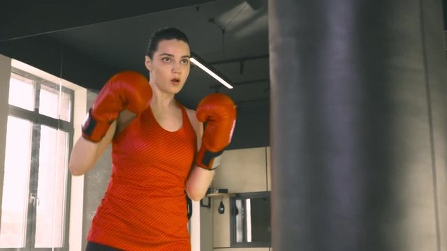 Young woman in boxing gloves hitting a boxing bag
