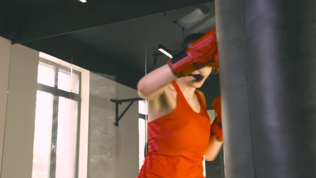 Young woman in boxing gloves hitting a boxing bag