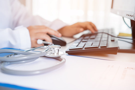 Healthcare and medical concept, Doctor working seaching information Patient database through internet computer, have Stethoscope with prescription clipboard record on hospital office, selective focus