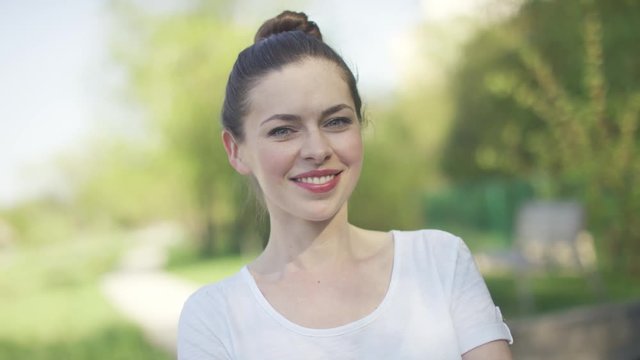 Young beautiful woman in white t-shirt smiling and looking at camera on blurred green background