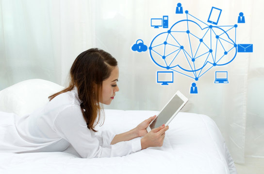 happy young asian woman in white pajamas using mobile tablet on bed in the morning at home and graphic network icon, smart communication technology, online shopping and payment online concept