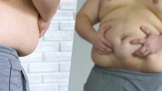 Unhappy obese male looking at his fat belly in mirror, weight loss, insecurities
