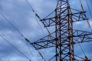 High voltage power pylons against blue sky and sun