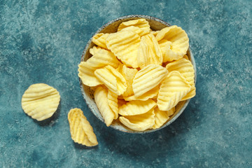 Crispy potato chips in bowl on a blue background. Food background, top view