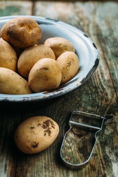 Raw potatoes in a bowl with Peeler 
