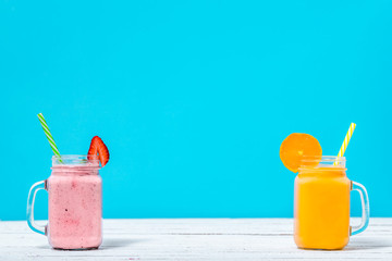 Summer refreshing smoothies with fruits, orange and strawberry smoothie in jar on blue background