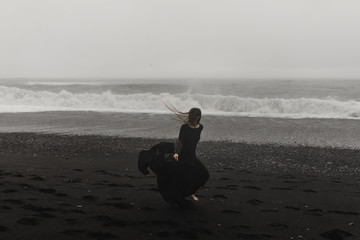 Fototapeta na wymiar woman wearing a black dress on the black beach in iceland during a storm