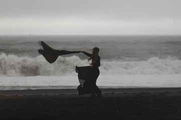 woman wearing a black dress on the black beach in iceland during a storm - 204635874