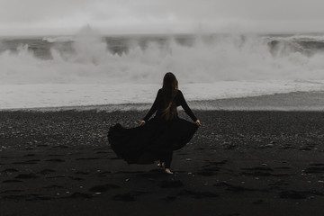 woman wearing a black dress on the black beach in iceland during a storm