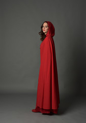 Naklejka premium full length portrait of woman wearing red fantasy costume with cloak, standing pose on grey studio background.