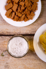 on a wooden table is a mug of foaming beer. in the background a white plate with crispy croutons. view from above. vertical photo.
